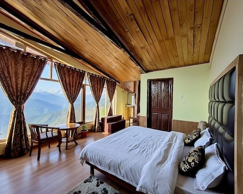 Guest bedroom with wooden sloped ceiling and panoramic windows overlooking Himalayan peaks